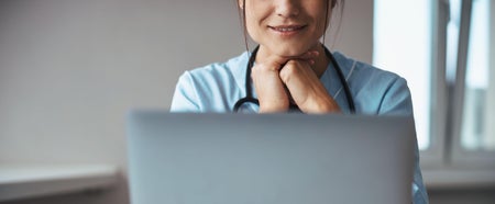 Female doctor with stethoscope around her neck smiles at patient during virtual visit.