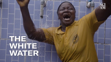 A woman, yelling triumphantly, looks toward the viewer as water splashes down onto her