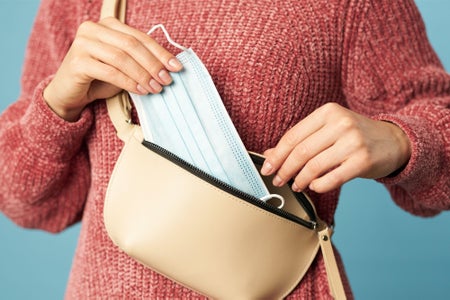 Woman in sweater removing face mask from sling bag/purse