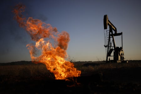 A natural gas flare burns near an oil pump jack.