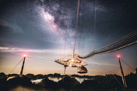 A view of the Arecibo Observatory's giant reflector dish and radio transmitter against a starry sky