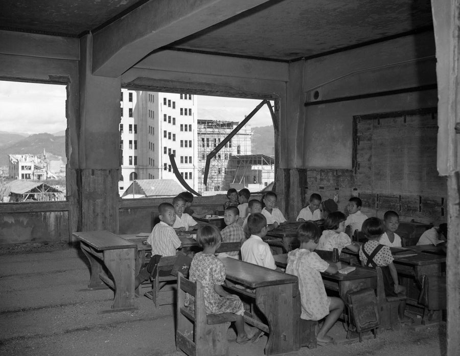 Children sit at school desks inside a partially destroyed building in Hiroshima one year after a nuclear weapon was dropped on the city