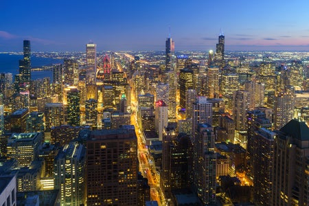 Aerial night view of city shows skyscrapers and busy streets.