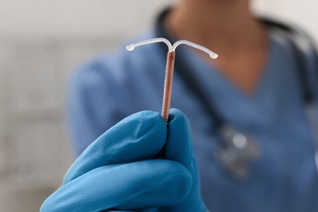 Doctor holding T-shaped intrauterine birth control device on blurred background, closeup