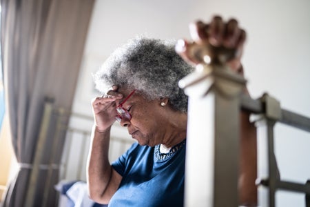 Senior woman with blue shirt sitting in a hot bright apartment on her bed at home.