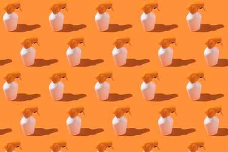 Pattern of white and orange bottles of sunscreen cream with spray on an orange background.