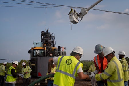 Energy workers with hard hats and yellow vests restoring powerlines