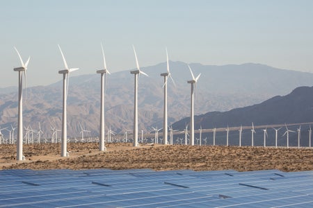 Solar panels and wind turbines in the California desert with mountains in the background.