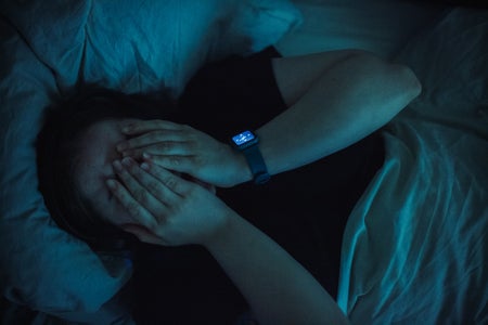 Tired young woman covering her face with hands while lying in bed at night