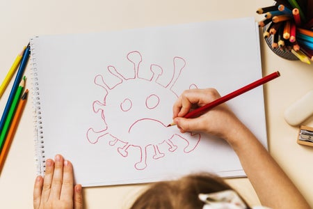 A small child draws a frowning coronavirus using red colored pencil, top view