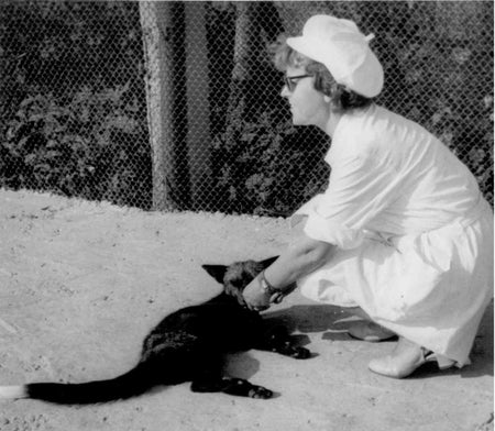 A black and whit photo showing a woman crouching to interact with a fox.