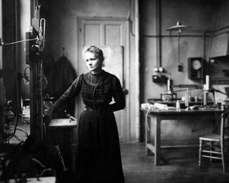 A black and white photograph showing Marie Curie standing in a science laboratory.