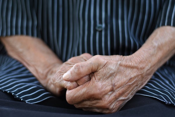 midsection of an old woman, hand in hand in lap, wearing black short with white straps