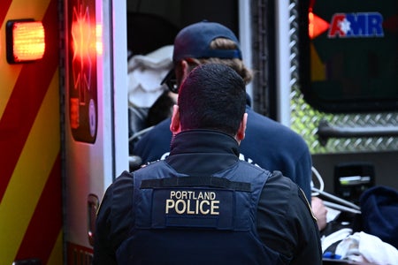 Photograph of the back of a Portland police officer as they watch an EMT help a patient inside an ambulance in Portland, Oregon