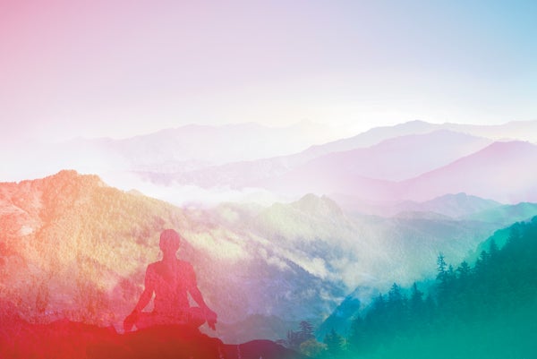 A person sitting in meditation pose in with a mountain landscape in the background.