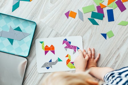 Close up of child playing with and creating simple images of animals with 2-D geometric shapes