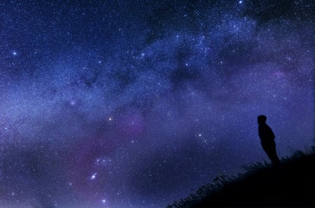 Silhouette of a man looking at the stars on a hill.