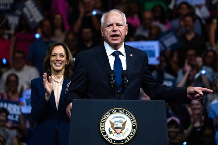 Tim Walz at podium with Vice President Kamala Harris clapping and spectators and in background.