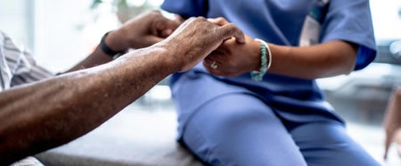 Two people holding hands, one sitting down and wearing scrubs