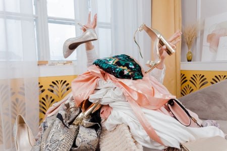 Woman hands out of a pile of clothes and accessories on the floor.